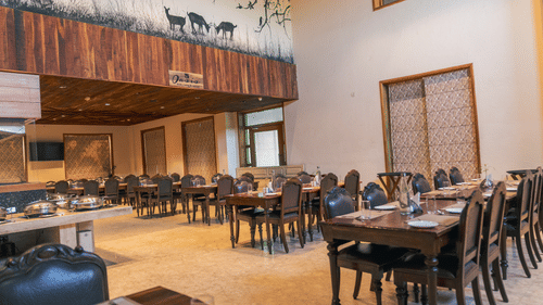 Oasis Restaurant dining area with tables and chairs arranged and a buffet counter on the side inside The Baagh Ananta Elite, Ranthambore.